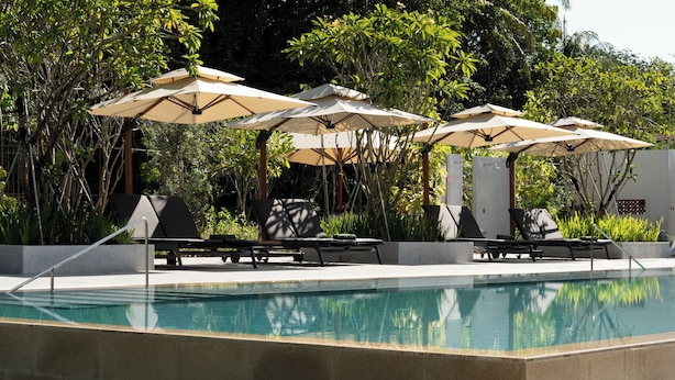 A pool area with lounge chairs and umbrellas, surrounded by greenery.