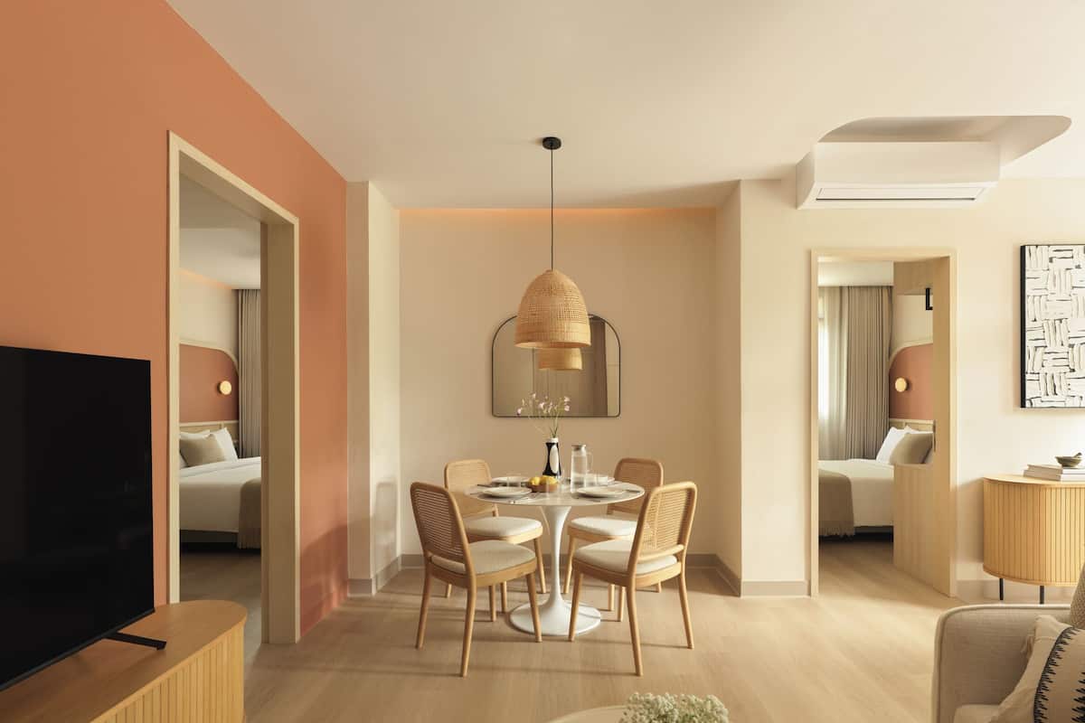 Una habitación de hotel moderna con una televisión de pantalla plana, una zona de comedor con una mesa redonda y sillas, un espejo grande y un sofá.