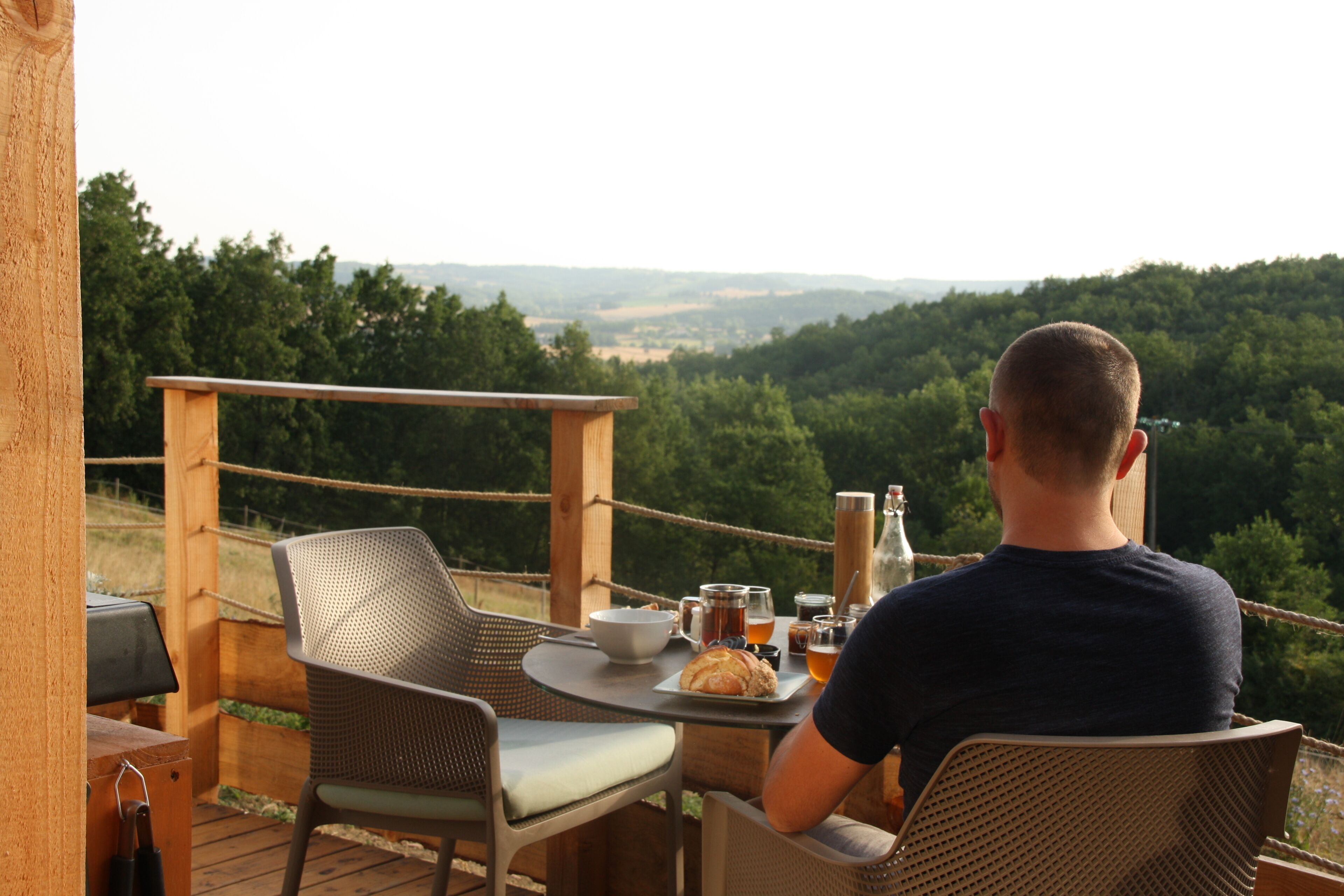 A man seated at an outdoor table with a view of a forested landscape.