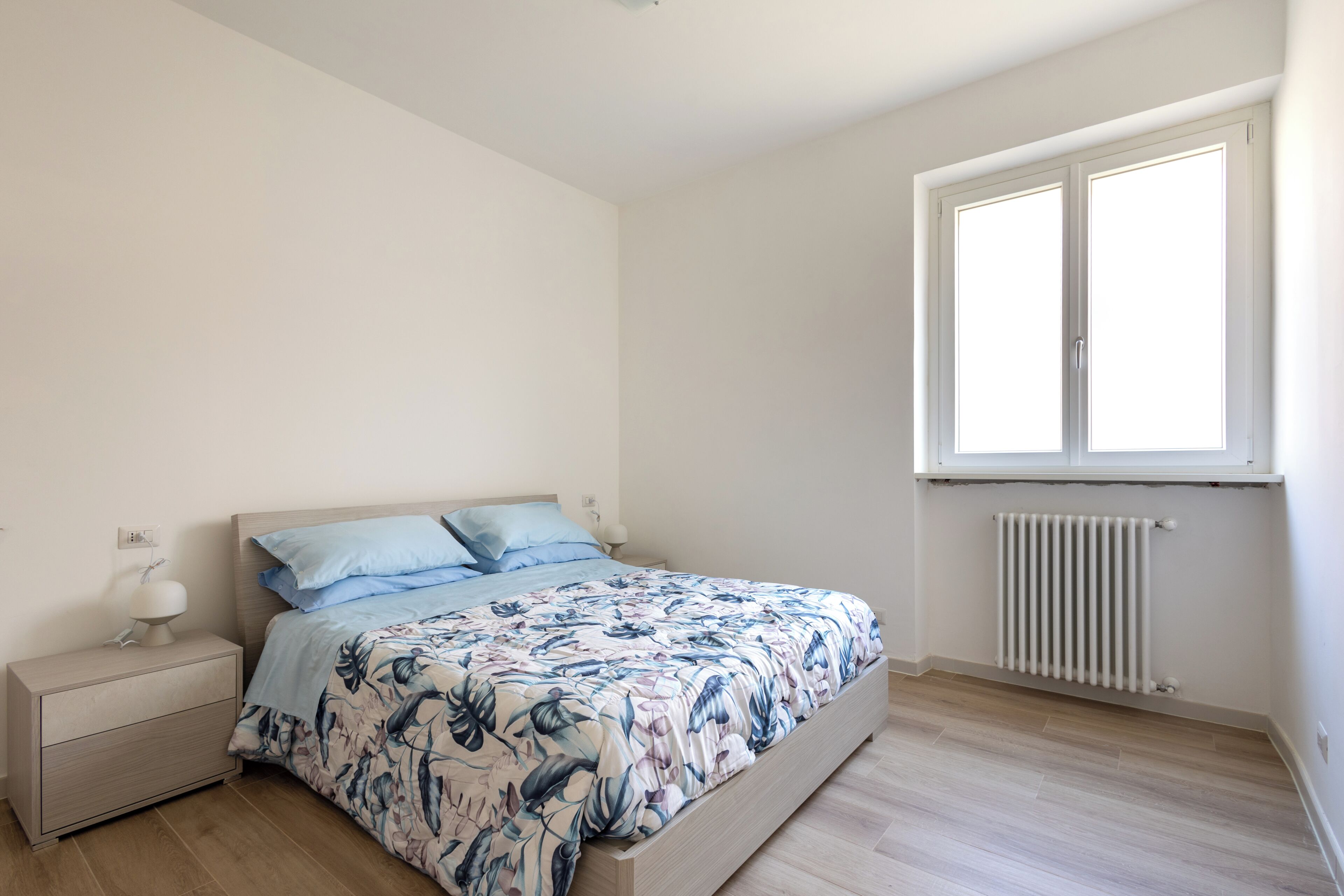Un dormitorio con cama, mesita de noche y ventana.