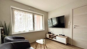 A modern living room with a flat-screen TV, a sofa, a small coffee table, and a cabinet. - New Apartment Just 1 Min from the Basel Border (Saint-Louis)