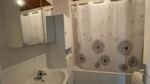 Een badkamer met een badkuip, een wastafel, een spiegel en een douchegordijn met een leeuwendanspatroon.