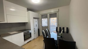 Une cuisine compacte dotée d’appareils électroménagers modernes, un coin repas avec une table et des chaises, et une vue sur un balcon extérieur accessible par une porte.
