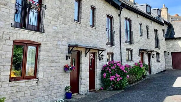 Un bâtiment en pierre avec des portes numérotées, des balcons dotés de rampes et des plantes en pot.