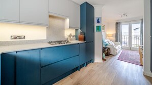 Une cuisine moderne avec des meubles bleus, une cuisinière à gaz et une vue sur un balcon.