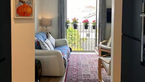 Un salon avec un canapé, une lampe, un tapis à motifs et un balcon agrément é de plantes en pot.