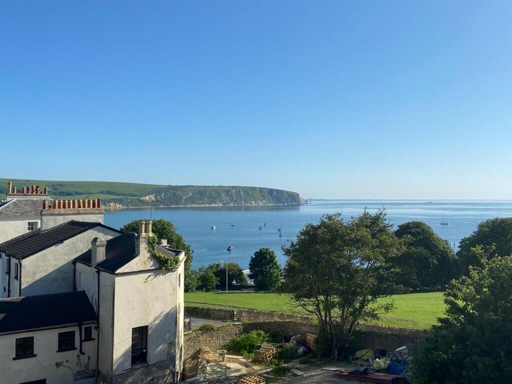 A coastal view with buildings, a grassy area, and a clear sky.