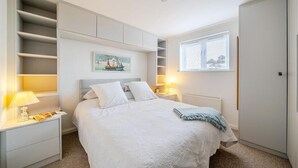 Une chambre à coucher comprenant un lit, des tables de chevet, un radiateur, une fenêtre avec stores et des étagères intégrées.