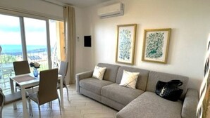 A modern living room with a sofa, a dining table with chairs, and two framed artworks on the wall. - Affittimoderni Red Island Elite PATI16 (Trinità d´Agultu e Vignola)