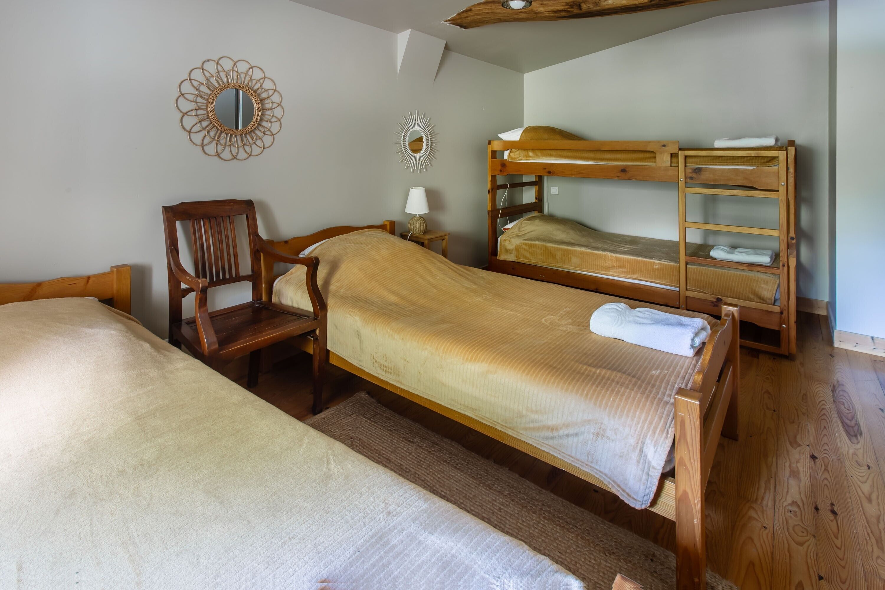 Une pièce avec deux lits superposés en bois, une chaise en bois, une petite table avec une lampe et un miroir accroché au mur.