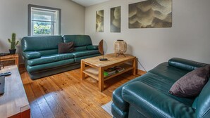 A living room with a green sofa, a wooden coffee table, a lamp, and artwork on the wall. - Holiday Home 'Aux Agapanthes', Shared Pool, Private Terrace, Landscaped Park, Free Wi-Fi (Aumagne)