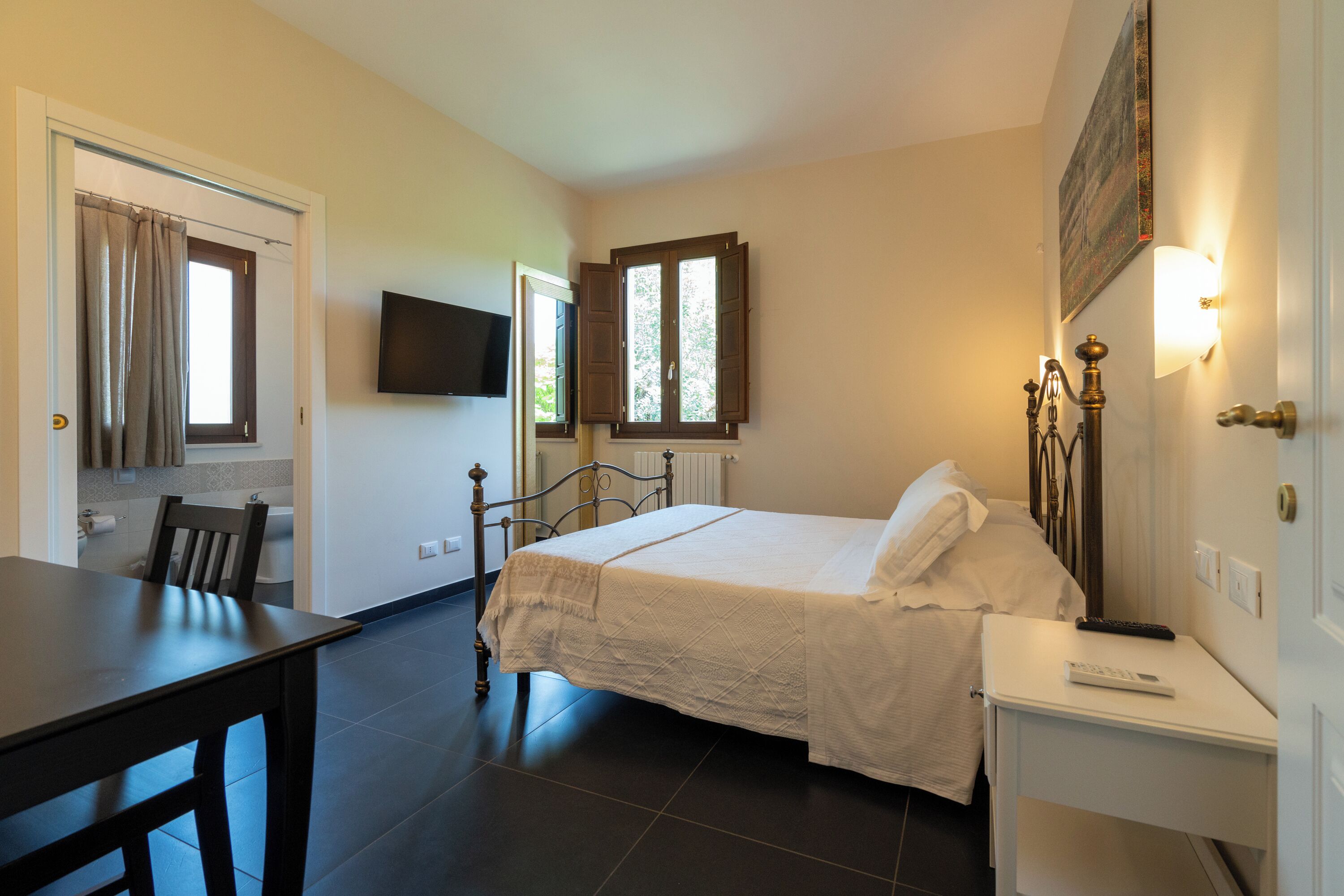 A bedroom with a bed, a bedside table, a chair, a TV mounted on the wall, and a window with curtains.