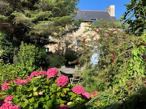 A stone building with a sloped roof, surrounded by lush greenery and vibrant pink flowers. - Bed and Breakfast 'Ti Brao - Curie' with Shared Garden and Wi-Fi (Penvénan)