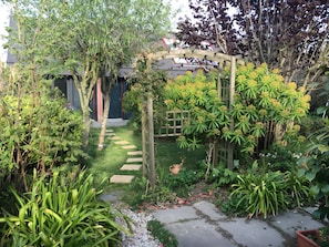 Un jardín con un arco de madera, un camino de piedra y diversas plantas.