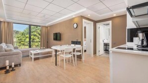 Een moderne hotelkamer met een zithoek, kitchenette en een groot raam met uitzicht op groen.