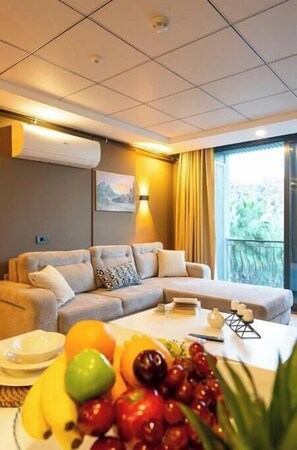 Ein modernes Hotelzimmer mit einer Couch, einem Esstisch mit Obst und einem großen Fenster.