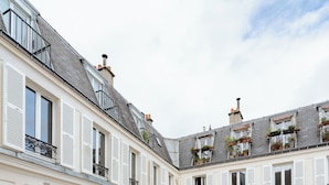 A multi-story building with white shutters, balconies with potted plants, and a courtyard. - Parisian Muse, by Veeve (Paris)