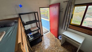 Una habitación pequeña con una cama, una estantería, un escritorio, una puerta roja y una ventana.