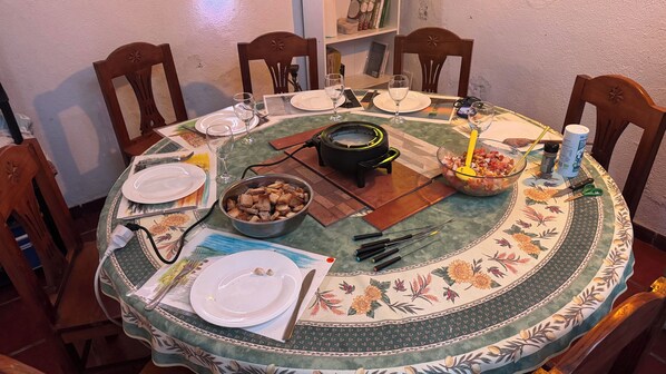 A dining table set with plates, glasses, cutlery, a bowl of food, a portable stove, and a water bottle.