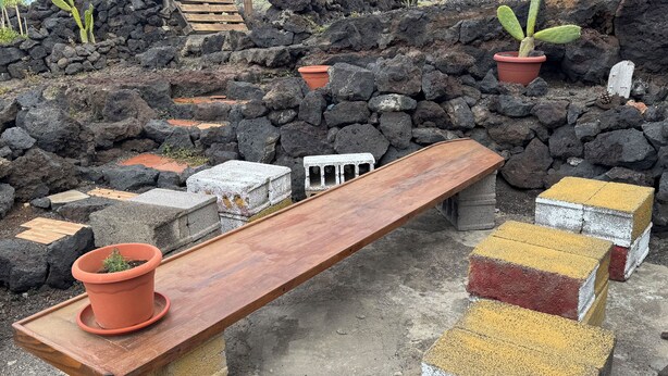 A wooden bench with a potted plant, surrounded by lava rocks and concrete blocks. - 7 Calcosas (Valverde)