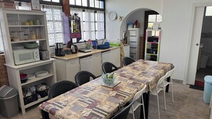 A compact kitchen with a microwave, toaster, and coffee maker on the counter, a dining table with a patterned tablecloth, and a window with curtains. - 7 Calcosas (Valverde)