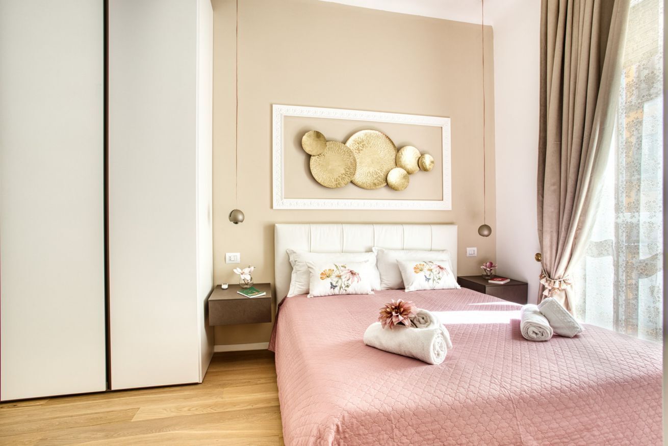 Une chambre à coucher comprenant un lit, une table de chevet, une œuvre d’art accrochée au mur et une fenêtre avec des rideaux.