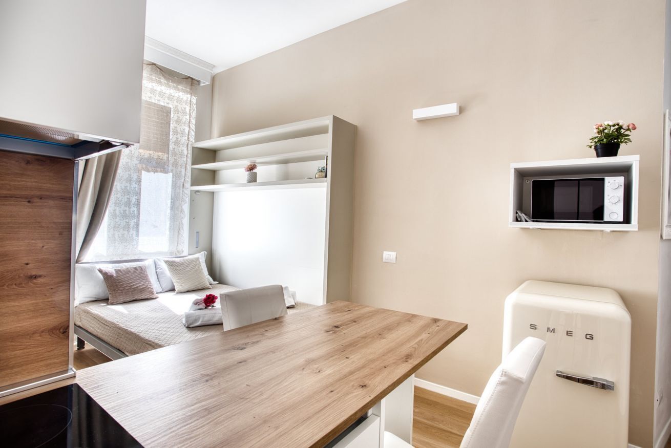 A modern room with a wooden table, a white sofa, a built-in shelf, a white microwave, and a small potted plant.