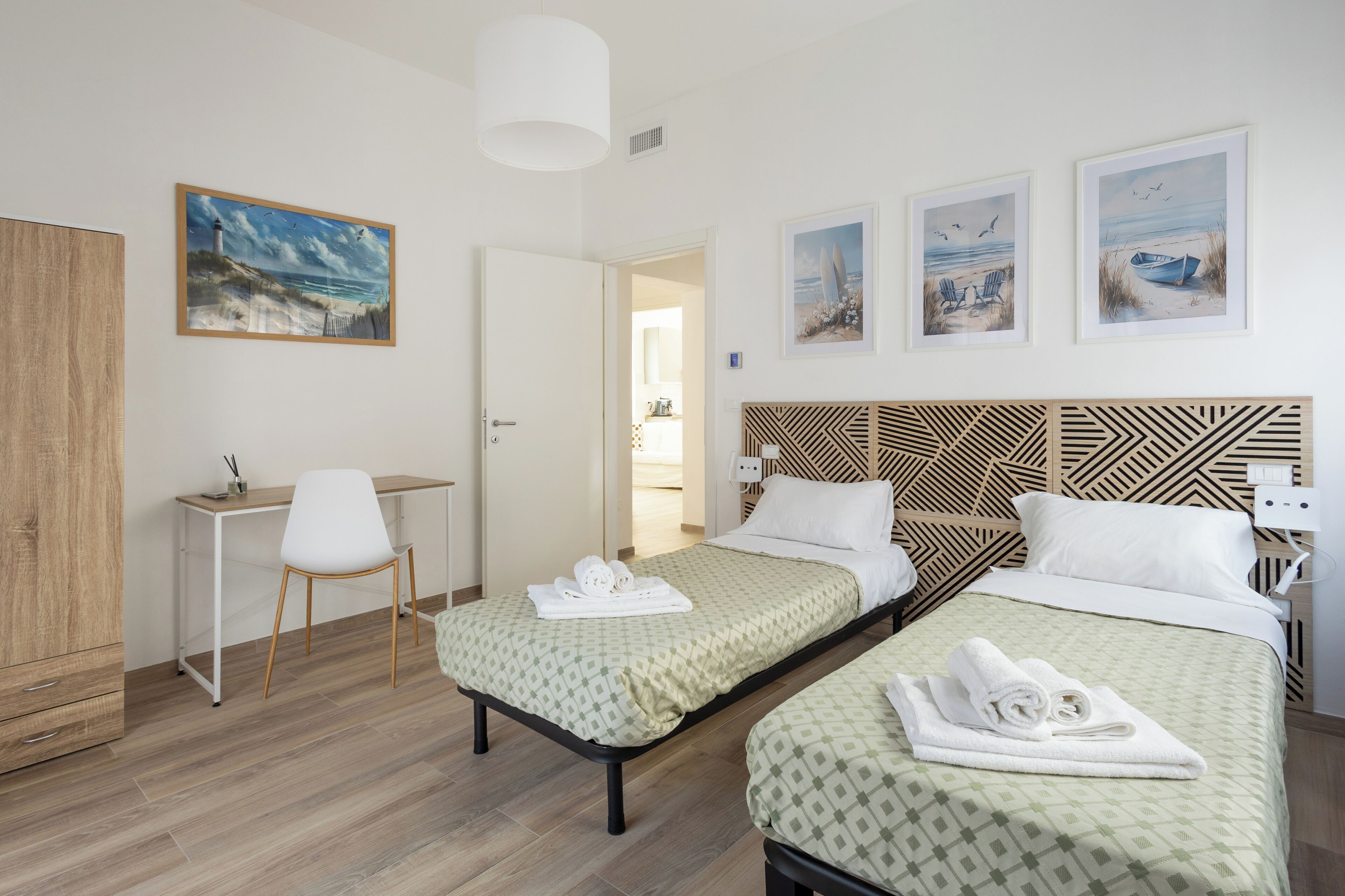 Une chambre d’hôtel avec deux lits, un bureau, une chaise et des œuvres d’art accrochées aux murs.