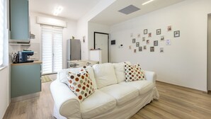 A modern living room with a sofa, a kitchen area, and a wall with pictures. - Nadia Flat - 10 minutes from the beach (Montesilvano)