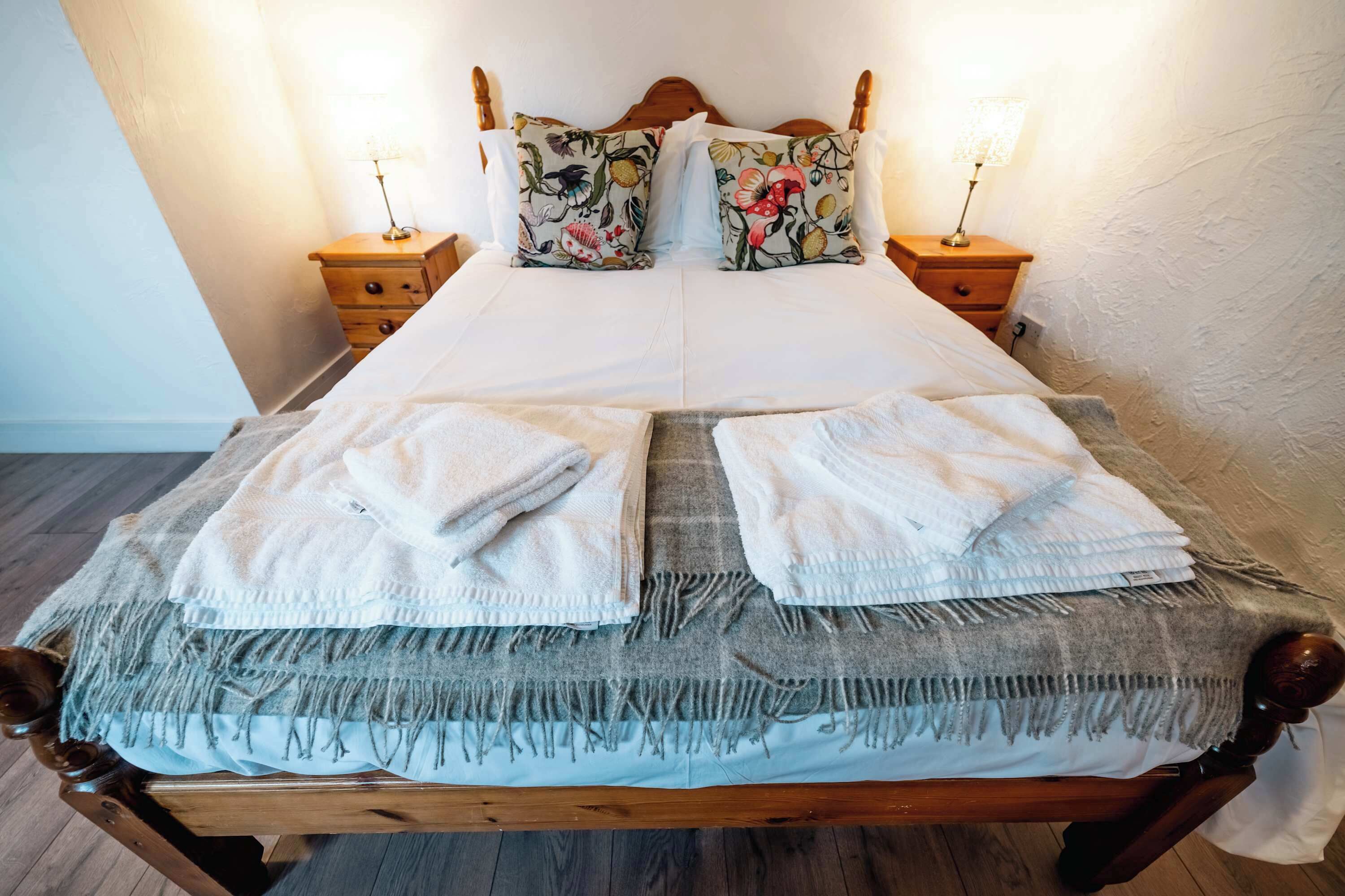 A neatly made bed with floral pillows, a wooden headboard, and two bedside tables with lamps.
