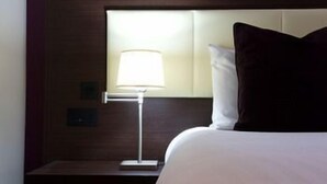 A hotel room with a bed, a nightstand, a lamp, and a window. - Hallmark Hotel Cambridge (Cambridge)