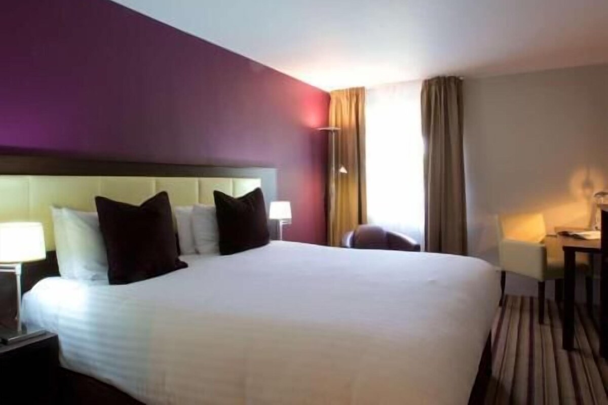 A hotel room with a large bed, a nightstand, a desk, and a chair.