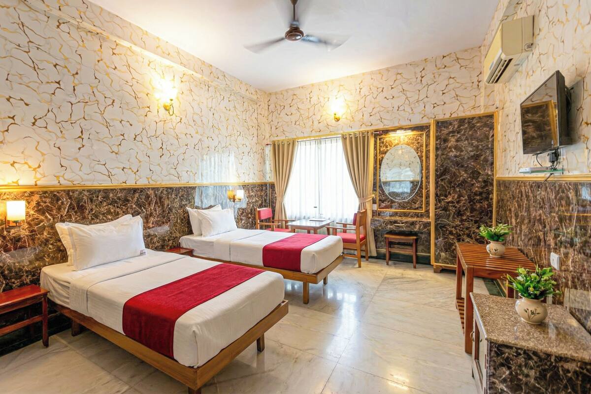A hotel room with two beds, a desk, a chair, a TV, and a ceiling fan.