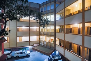 A multi-story building with a courtyard, featuring a car parking area and a tree.