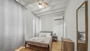 Ein Schlafzimmer mit Holzboden, einem Bett mit Kopfteil, einem Nachttisch, einem Beistelltisch, einem Spiegel und einer Klimaanlage.