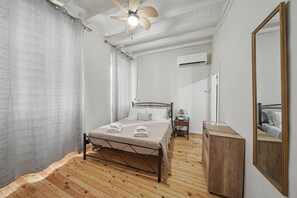 Ein Schlafzimmer mit Holzboden, einem Bett mit Kopfteil, einem Nachttisch, einem Beistelltisch, einem Spiegel und einer Klimaanlage.