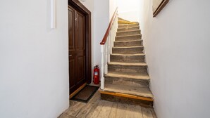 Eine Treppe mit Holzsitzen und weißen Geländern, eine braune Tür sowie ein roter Feuerlöscher.