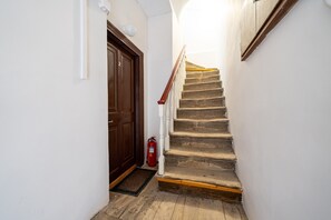 Eine Treppe mit Holzsitzen und weißen Geländern, eine braune Tür sowie ein roter Feuerlöscher.