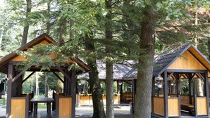 A wooden pavilion with benches and a picnic table, surrounded by trees.