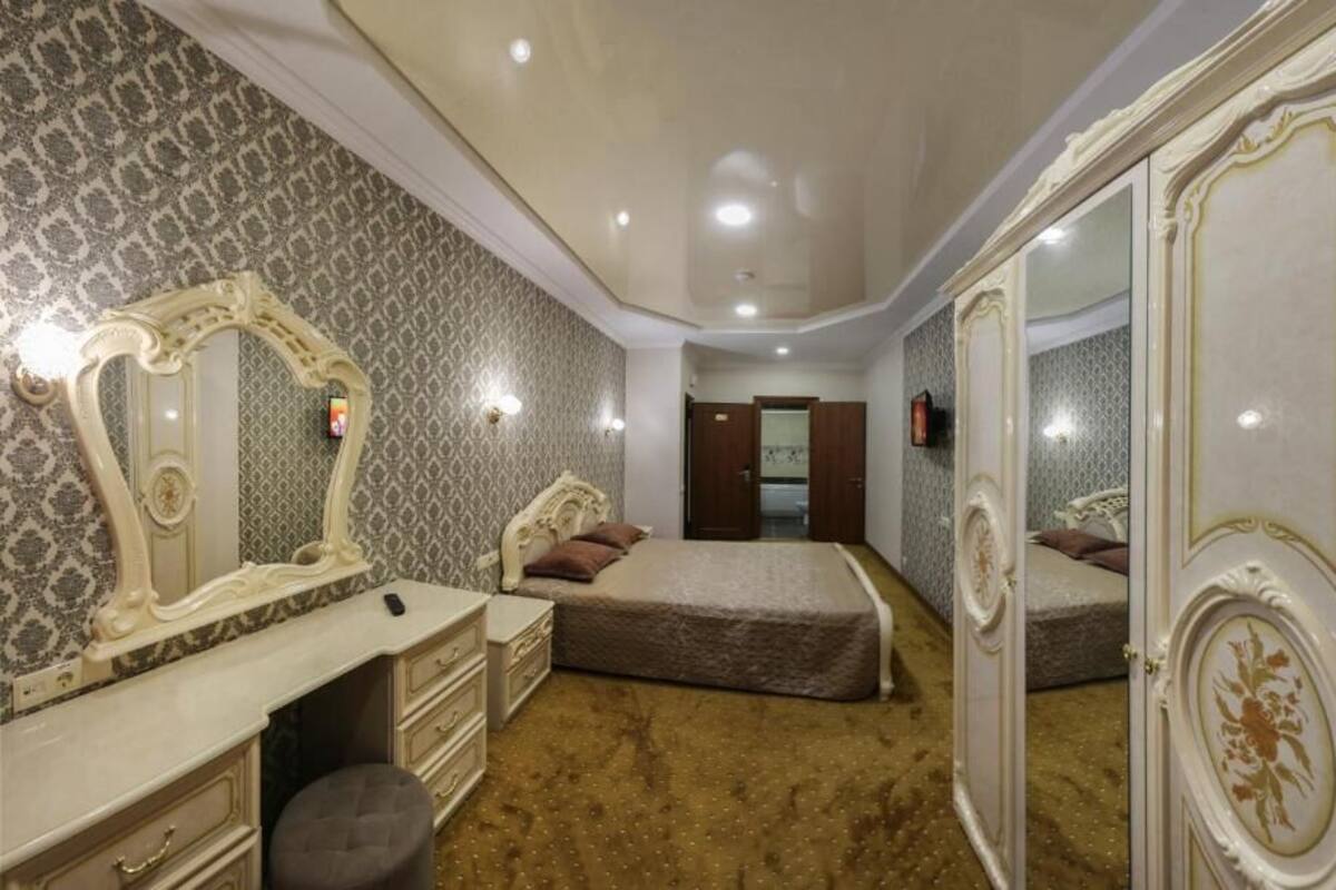 Ein Schlafzimmer mit einem Bett, einem Schminktisch, einem Spiegel und einer Tür zu einem weiteren Raum.