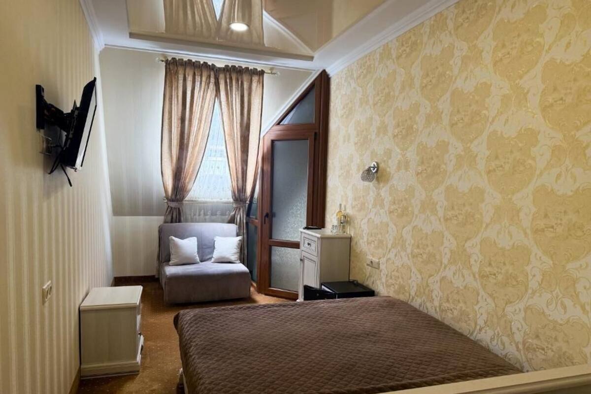 Ein Schlafzimmer mit Bett, Nachttisch, Kommode, einem Fenster mit Vorhängen und einem an der Wand montierten Fernseher.