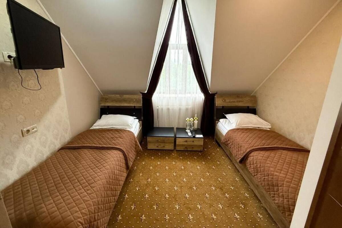Ein kleines Hotelzimmer mit zwei Betten, einem Fernseher, einem Fenster mit Vorhängen und einem kleinen Tisch mit einer Vase.