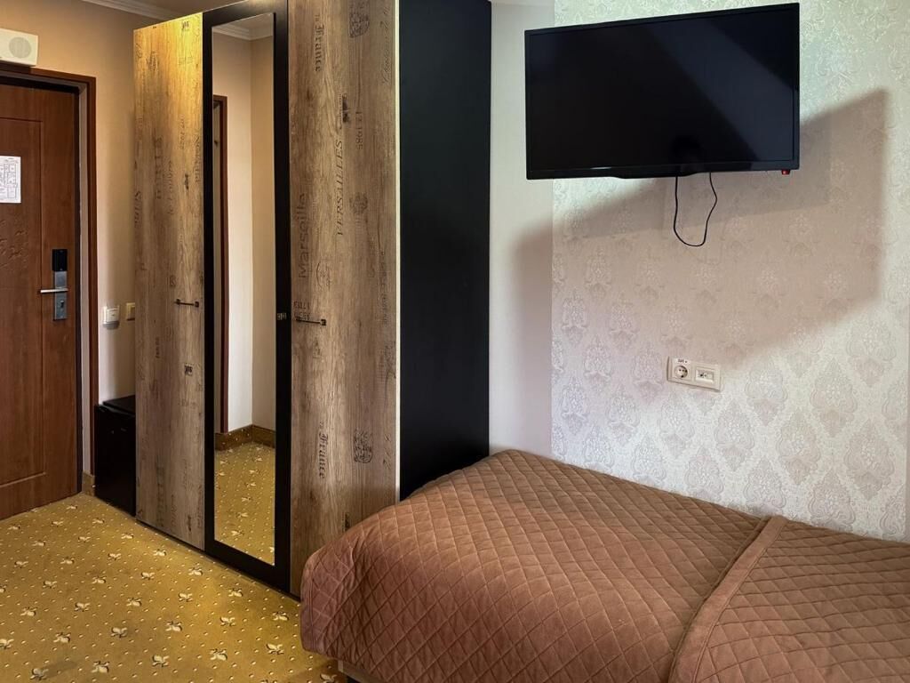 Un dormitorio con cama, televisor montado en la pared, espejo y puerta.