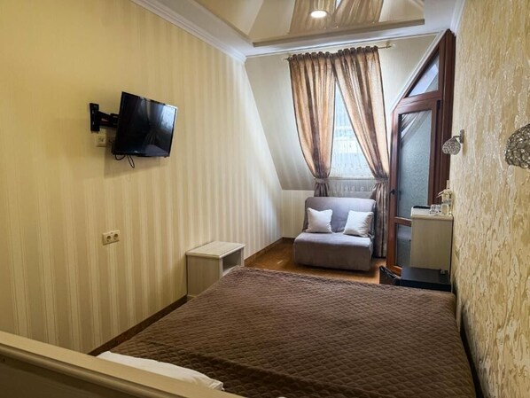 Une chambre à coucher avec un lit, un téléviseur fixé au mur, une fenêtre avec des rideaux et une petite table de chevet.