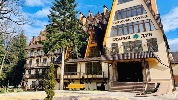A multi-story building with a distinctive triangular roof, a staircase leading to the entrance, and a bench outside.
