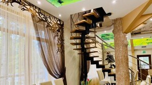 A dining area with a staircase, tables, chairs, and a decorative tree trunk.