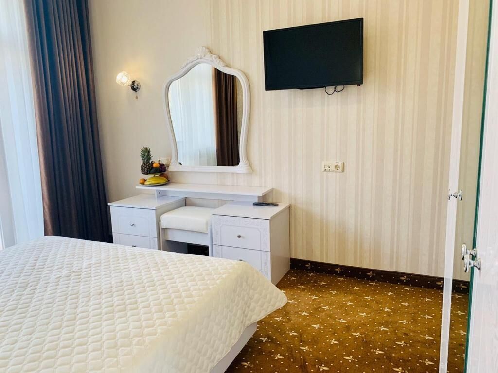 Camera d'albergo con un letto, una cassettiera bianca, uno specchio, una televisione a schermo piatto e una porta.