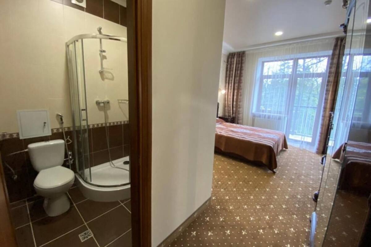 Ein Badezimmer mit Dusche, Toilette und Waschbecken; ein Schlafzimmer mit Bett und Fenster; und ein Flur mit Spiegel.