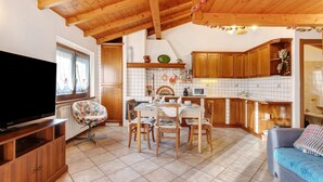 Una sala de estar acogedora con televisor, muebles de madera, un comedor y una cocina con alacenas de madera y salpicadero de azulejos.