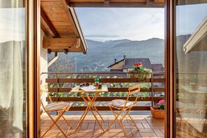 Een balkon met een houten tafel, twee stoelen en uitzicht op bergen.